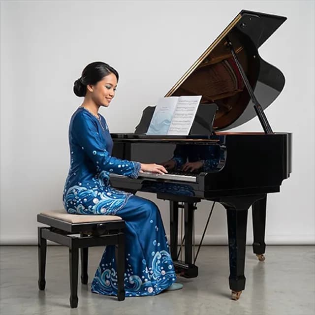 Piano teacher in a blue floral baju kurung playing a grand piano, with sheet music on the stand